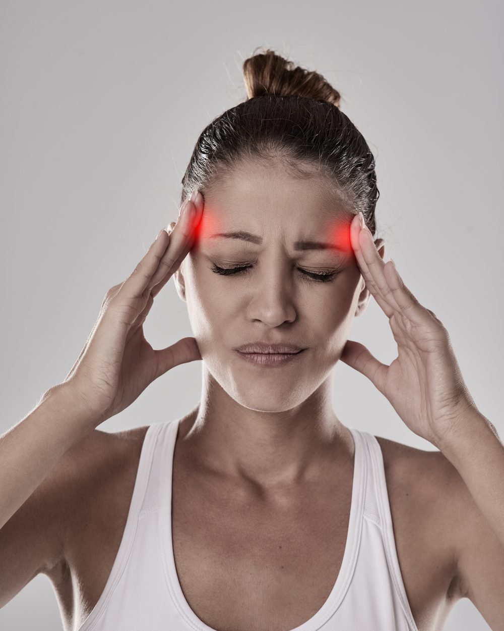 Mulher de olhos fechados pressionando as têmporas com as duas mãos, com as regiões doloridas destacadas em vermelho